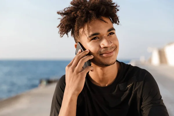 Close up of a young african sportsman at the beach, talking on mobile phone