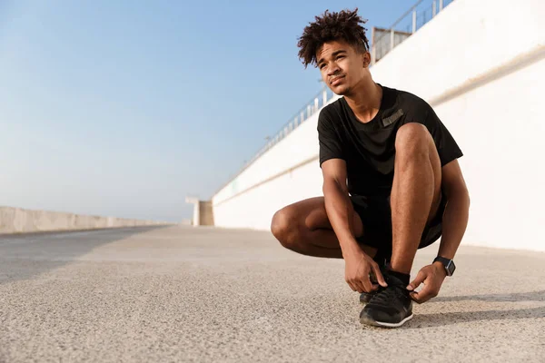 Joven Africano Confiado Vestido Con Ropa Deportiva Atándose Cordón Playa — Foto de Stock