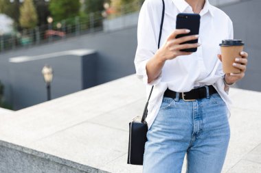 Genç bir kadının sokakta ayakta, kahve holding, cep telefonuyla görüntü kırpılmış