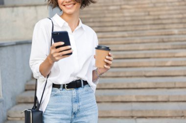 Sokakta cep telefonuyla kahve tutan genç inanılmaz kadın fotoğrafı kırpılmış.