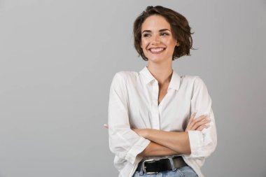 Gri duvar arkasında yalnız poz veren mutlu genç iş kadını görüntüsü.