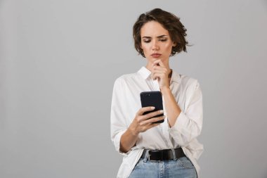 Genç iş kadını cep telefonu sohbet kullanarak gri duvar arka plan üzerinde izole poz resim düşünme karıştı.