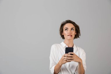 Genç iş kadını cep telefonu sohbet kullanarak gri duvar arka plan üzerinde izole poz resim düşünme karıştı.