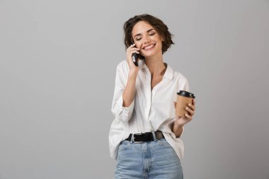 Kahve içme cep telefonuyla konuşurken gri duvar arka plan üzerinde izole görüntüsünü poz mutlu genç iş kadını.