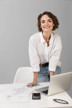 Dizüstü yakınındaki masada gri duvar arka plan üzerinde izole görüntüsünü poz genç iş kadını.