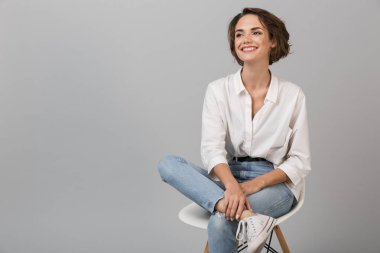 Taburede oturan gri duvar arka plan üzerinde izole görüntüsünü poz genç iş kadını.