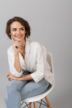 Taburede oturan gri duvar arka plan üzerinde izole görüntüsünü poz genç iş kadını.