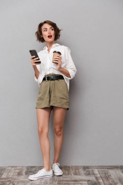 Tam boy görüntü genç Avrupa kadın 20'li yaşlarda holding paket servisi olan restoran kahve ve gri arka plan üzerinde izole smartphone kullanarak