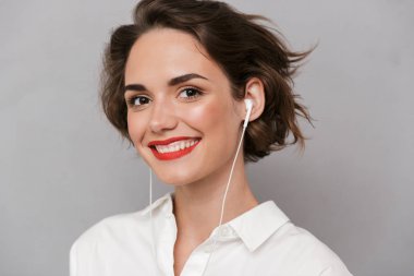 Gri arka plan üzerinde izole kamera gülümseyen güzel kadın 20'li yaşlarda giyen beyaz kulaklık fotoğrafı