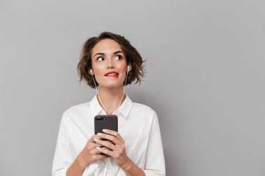Beyaz kadın 20'li yaşlarda fotoğrafı Smartphone cep telefonu ile gri arka plan üzerinde izole kulaklık ile müzik dinlemek