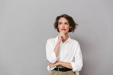 Dalgın bir genç kadının portresi ararken gri arka plan üzerinde izole ayakta beyaz gömlek giymiş