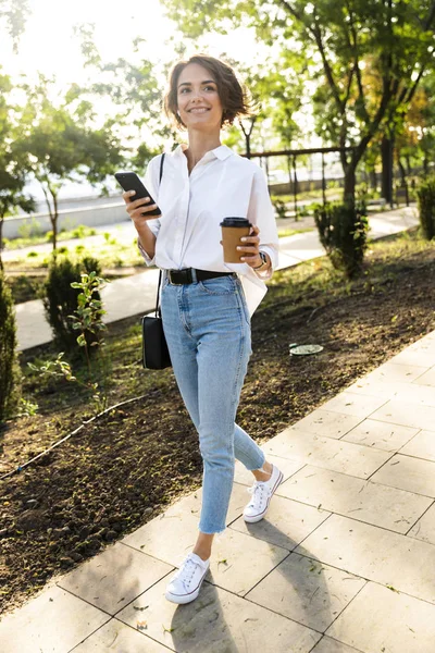 Preciosa Mujer Joven Caminando Por Calle Sosteniendo Teléfono Móvil Bebiendo —  Fotos de Stock