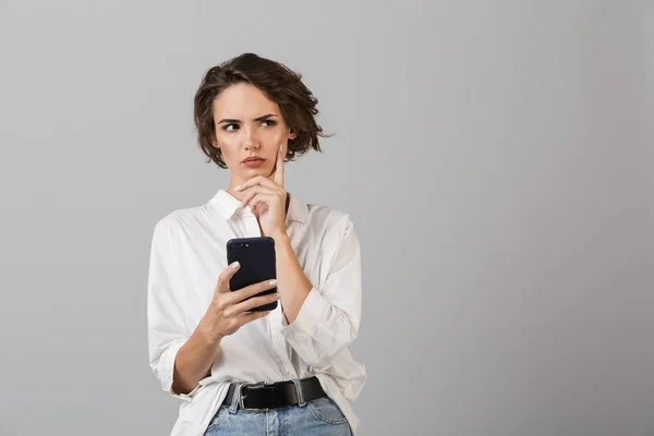 思考のイメージ混乱若いビジネス女性が携帯電話のチャットを使用して灰色の壁背景上孤立したポーズ — ストック写真