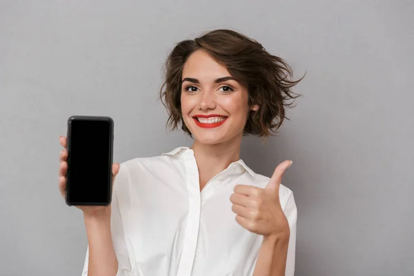 照片中美丽的女人20多岁拿着手机 并显示在灰色背景隔离的模仿屏幕 — 图库照片