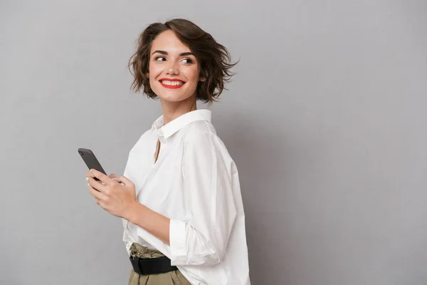 照片中迷人的女人20多岁微笑 拿着手机孤立在灰色背景 — 图库照片