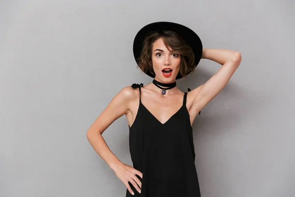 スタイリッシュな女性 代の身に着けている黒いドレスと帽子灰色の背景上分離カメラで笑顔の写真 — ストック写真