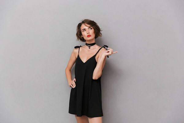 Photo of adorable woman 20s wearing black dress smiling at camera isolated over gray background