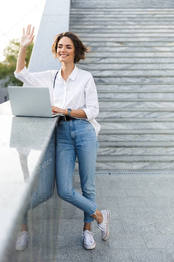 Picture of young cute beautiful woman walking outdoors using laptop computer.