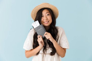 Genç heyecanlı Asyalı güzel kadın pasaport ve bilet tutan mavi arka plan üzerinde izole görüntüsünü.