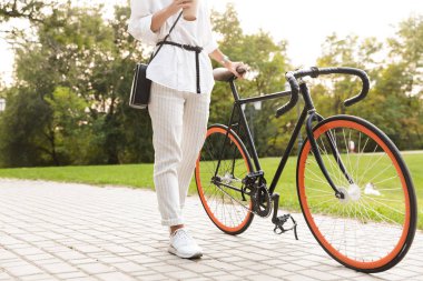 Genç kadın kahve tutan Bisiklet ile parkta yürüyüş fotoğrafı kırpılmış.