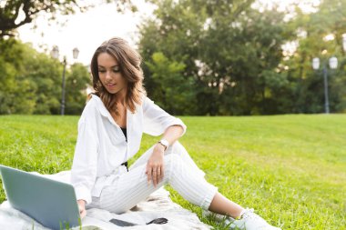Dizüstü bilgisayar kullanan bir çim üzerinde oturan parkta vakit güzel bayanı