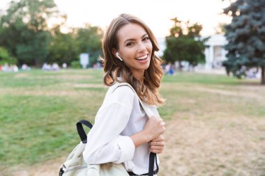 Görüntü neşeli sevimli genç kadının kameraya bakarak kulaklık ile müzik dinleme Bisiklet ile parkta yürüyüş.