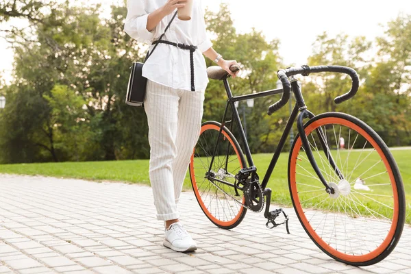 コーヒーを持って自転車で公園を歩いて若い女性の写真をトリミング — ストック写真