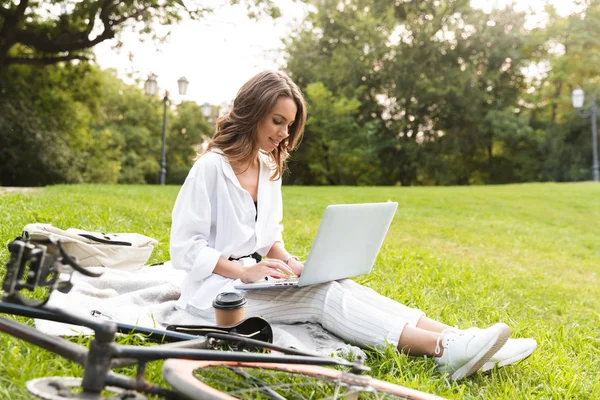 素敵な若い女性の自転車公園で時間を費やして 草の上に座って ラップトップ コンピューターを使用して — ストック写真