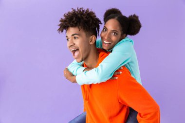 Genç kız kardeşi menekşe arka plan üzerinde izole sırtında taşıyan neşeli Afro-Amerikan kardeş fotoğrafı