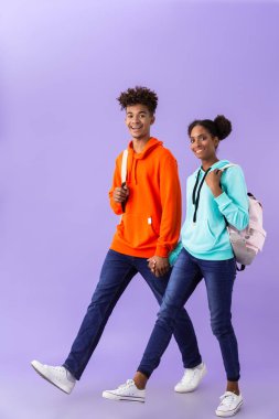 Tam boy fotoğrafı güzel Afrikalı-Amerikalı ve birlikte yürüyen sırt çantaları giyen kız menekşe arka plan üzerinde izole