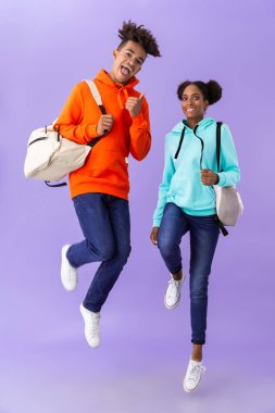 Mutlu Afro-Amerikan insanlar giyen fotoğrafı tam uzunlukta menekşe arka plan üzerinde izole gülen ve having fun sırt çantaları