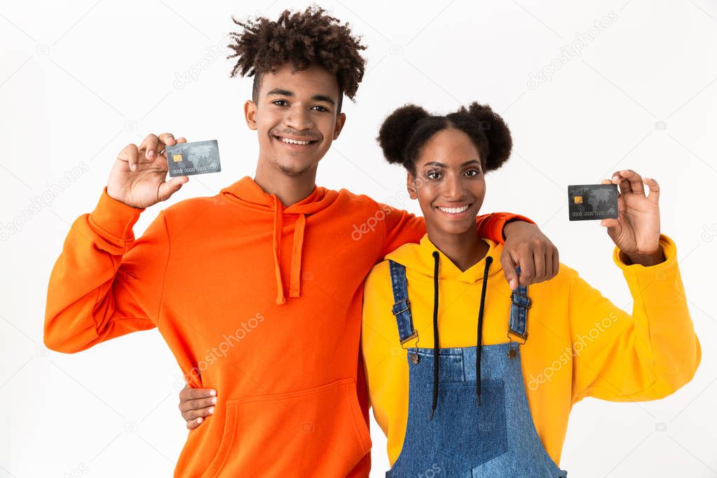 Photo of smiling african american couple standing together and holding credit cards isolated over white background