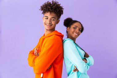 Neşeli Afro-Amerikan çift renkli giysiler izole mor arka plan üzerinde duran sırt sırta gülümseyen fotoğrafı