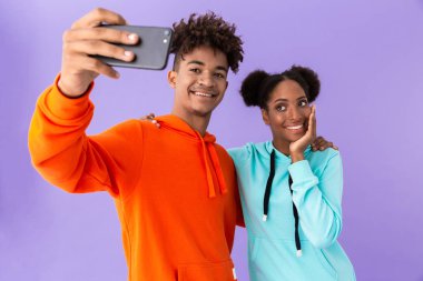 Menekşe arka plan üzerinde izole Smartphone cep telefonu ile selfie alarak renkli tişörtü giyen genç Afro-Amerikan çift fotoğraf