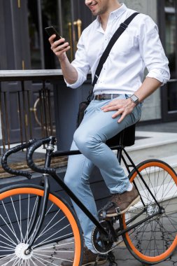 Cep telefonu tutan bir çanta taşıyor bir bisiklet açık havada, şehir cadde üzerinde oturan gömlek giymiş bir işadamı resim kırpılmış