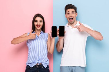 Görüntü gülümseyen adam ve kadın ayakta ve cep telefonları renkli arka plan üzerinde izole tutarak rahat kıyafet
