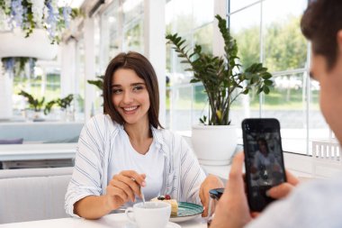 İnanılmaz genç sevgi dolu çift kafede oturup yemek tatlılar ve çay içme. Adam kız arkadaşını telefonla bir fotoğraf almak.