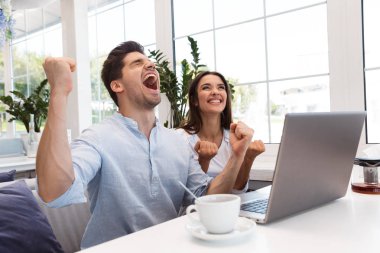 Kazanan jest yapmak imge-in inanılmaz heyecanlı genç sevgi dolu çift dizüstü bilgisayar kullanan kafede oturan.