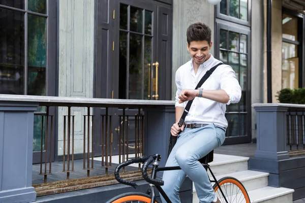 時間のチェック 袋を運ぶ街 屋外で自転車に乗ってのシャツを着ている陽気なビジネスマン — ストック写真