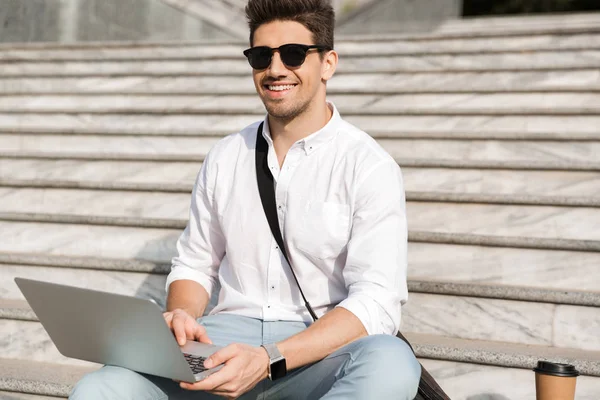 街の階段に座ってラップトップを使用してサングラスをかけて美しい男 代の写真 — ストック写真