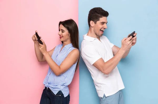 Young man and woman playing together video games using phones isolated over colorful background