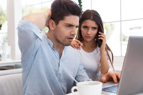 困惑的不高兴的年轻爱情夫妇坐在咖啡馆里 用笔记本电脑通过电话交谈的图像 — 图库照片