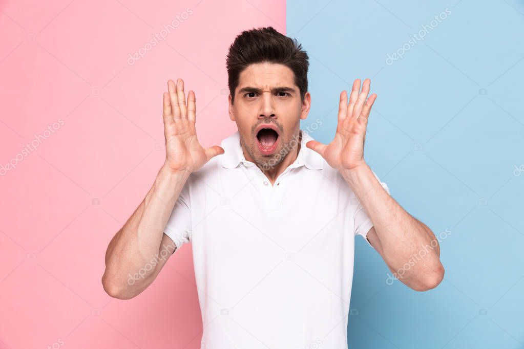Image of young man 20s wearing casual t-shirt screaming and raising arms isolated over colorful background