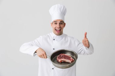 Görüntü izole kapalı tutan tava pişirme et beyaz duvar arka plan üzerinde heyecanlı genç adam şef.