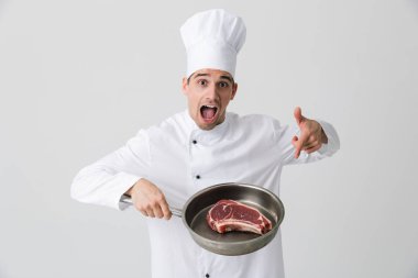 Görüntü izole kapalı tutan tava pişirme et beyaz duvar arka plan üzerinde heyecanlı genç adam şef.