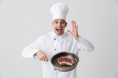 Görüntü izole kapalı tutan tava pişirme et beyaz duvar arka plan üzerinde heyecanlı genç adam şef.