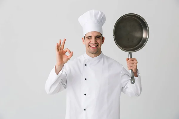 兴奋情绪激动的年轻人厨师在室内孤立在白色墙壁背景拿着煎锅的图片 — 图库照片