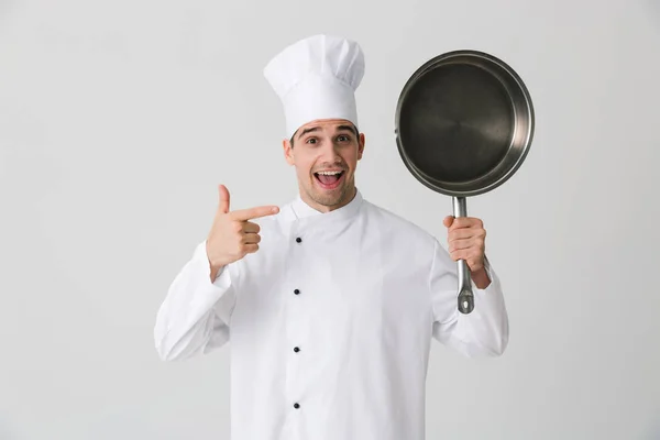 兴奋情绪激动的年轻人厨师在室内孤立在白色墙壁背景拿着煎锅的图片 — 图库照片