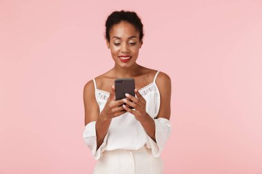 Cep telefonu kullaranarak pembe backgroung duvardan izole güzel genç Afrikalı kadın görüntüsünü.