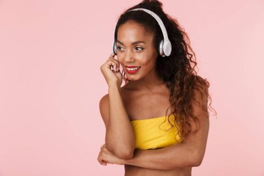 Görüntü izole kulaklık ile müzik dinleme pembe bir arka plan üzerinde mayo poz içinde neşeli genç kadın.